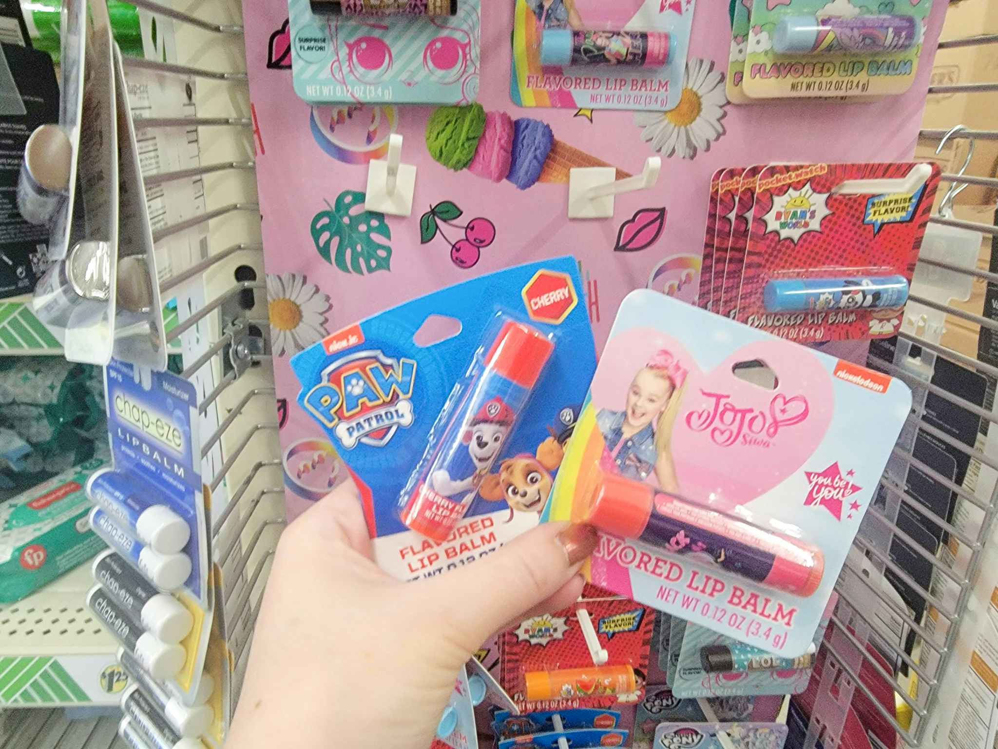 hand holding a paw patrol and a jojo siwa lip balm