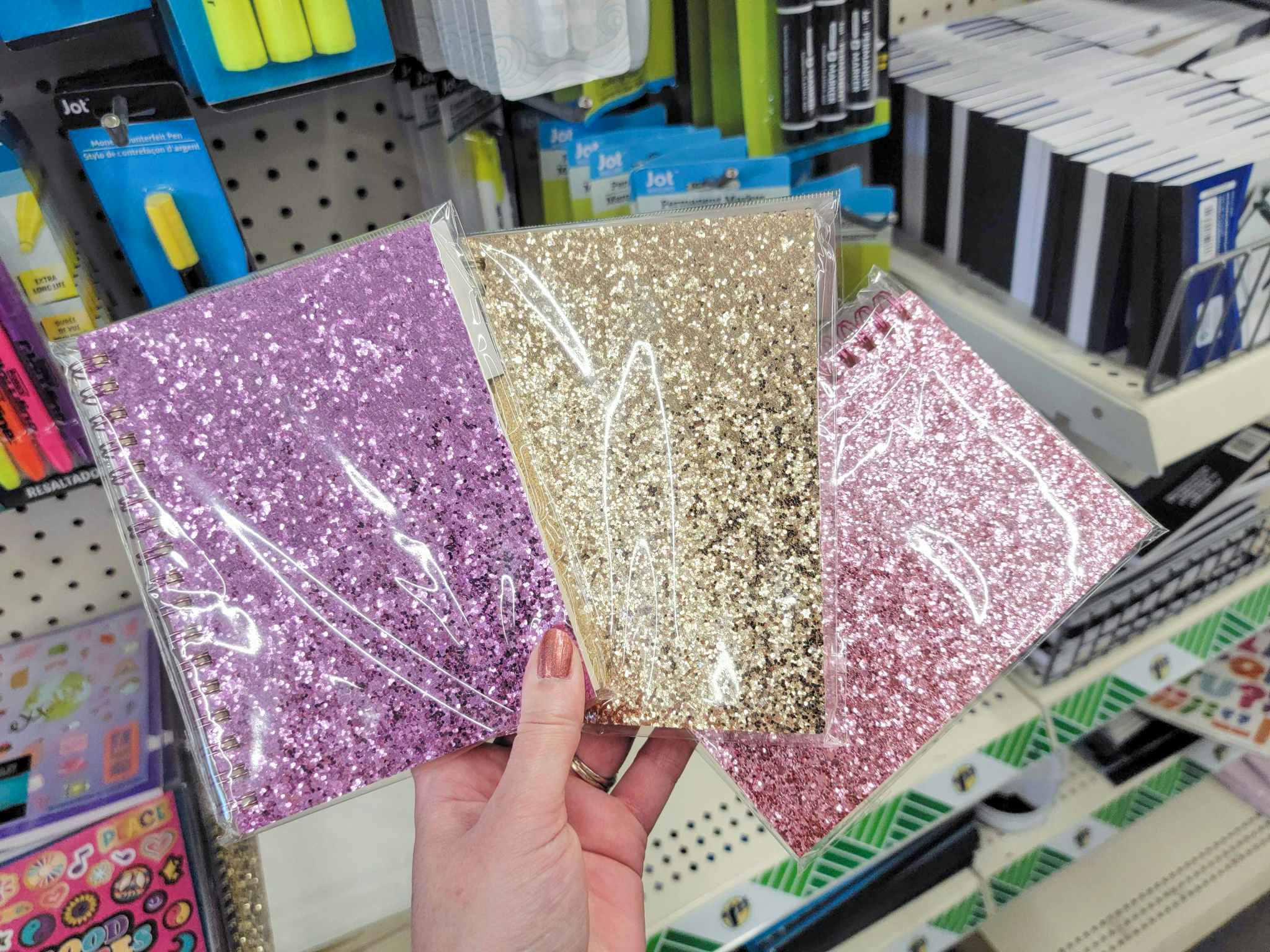 hand holding three glittery notebooks
