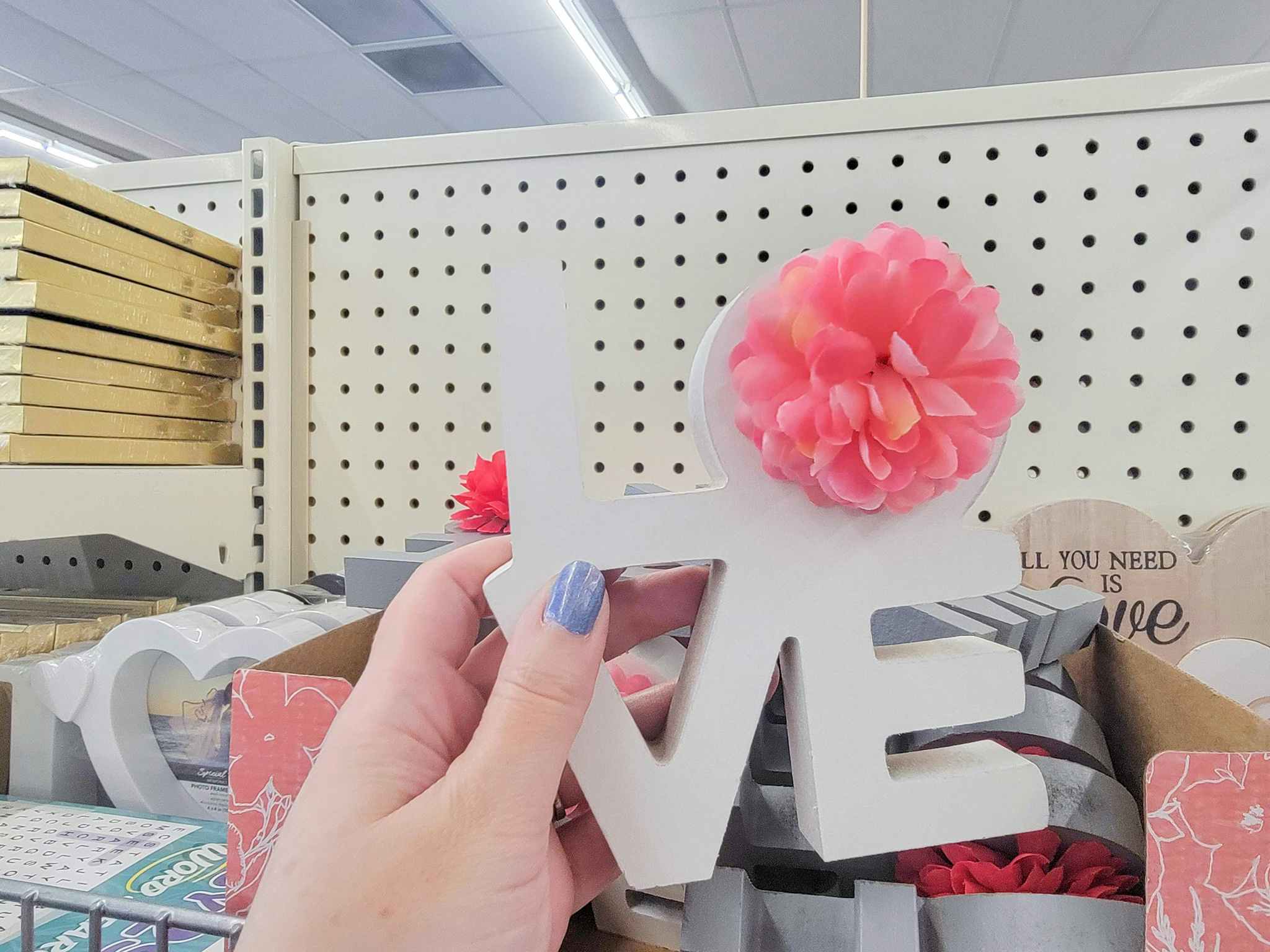 hand holding a white "love" table top decor with a pink flower on the "o