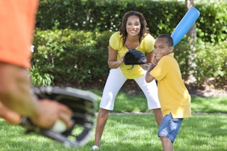 A woman standing in the grass holding a baseball glove, and a boy holding a baseball front standing to the left of her.
