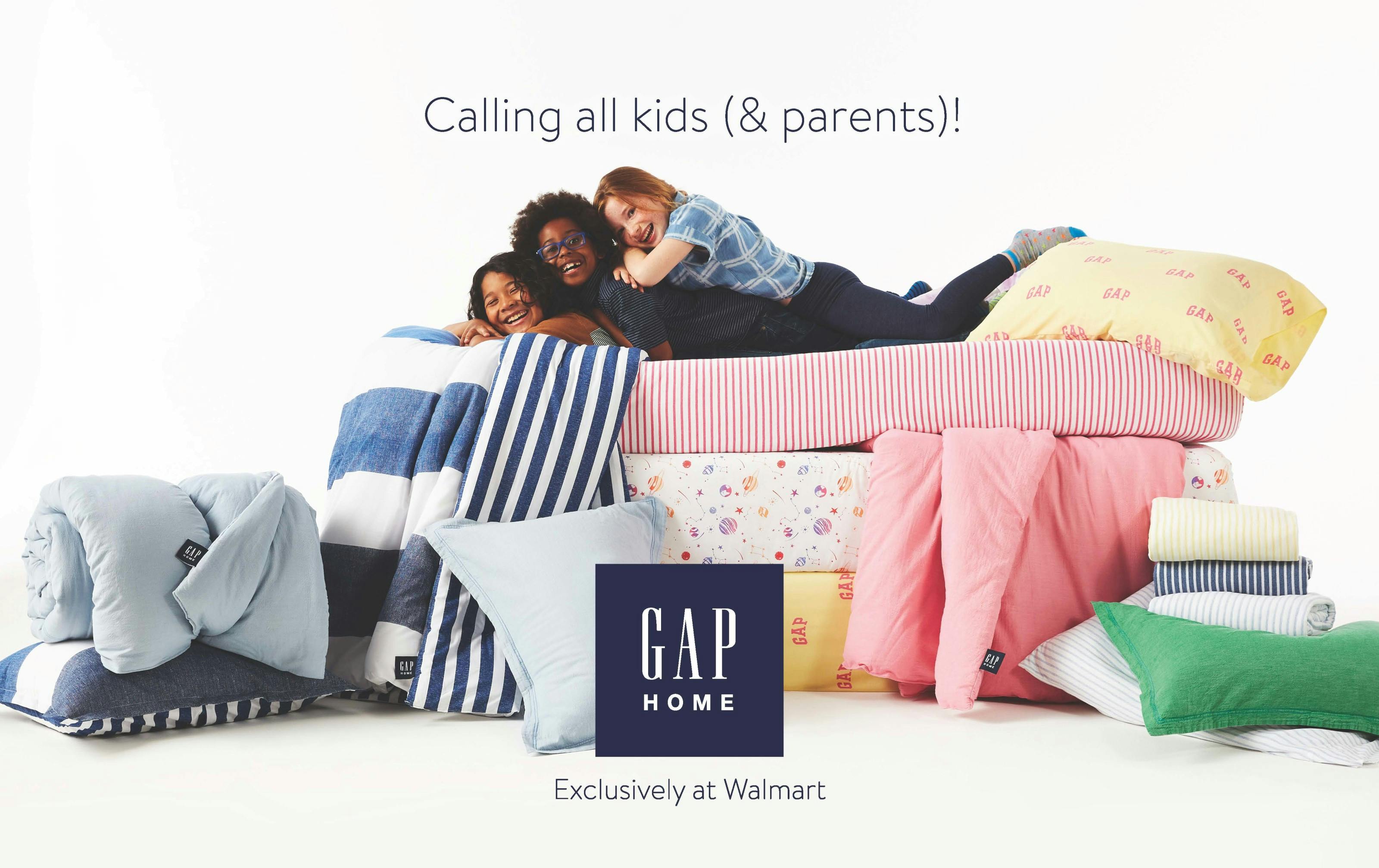 Kids stacked on top of each others backs laying on a bed full over colorful bedding and pillows.