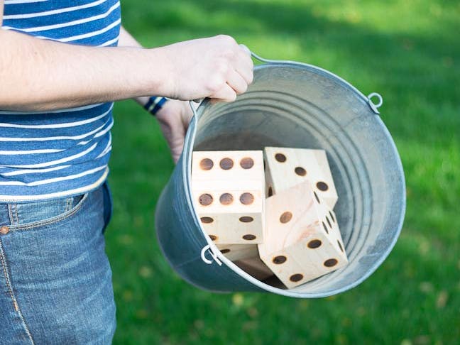 A person holding a bucket full of DIY giant dice, about to throw them for a yard Yahtzee game.