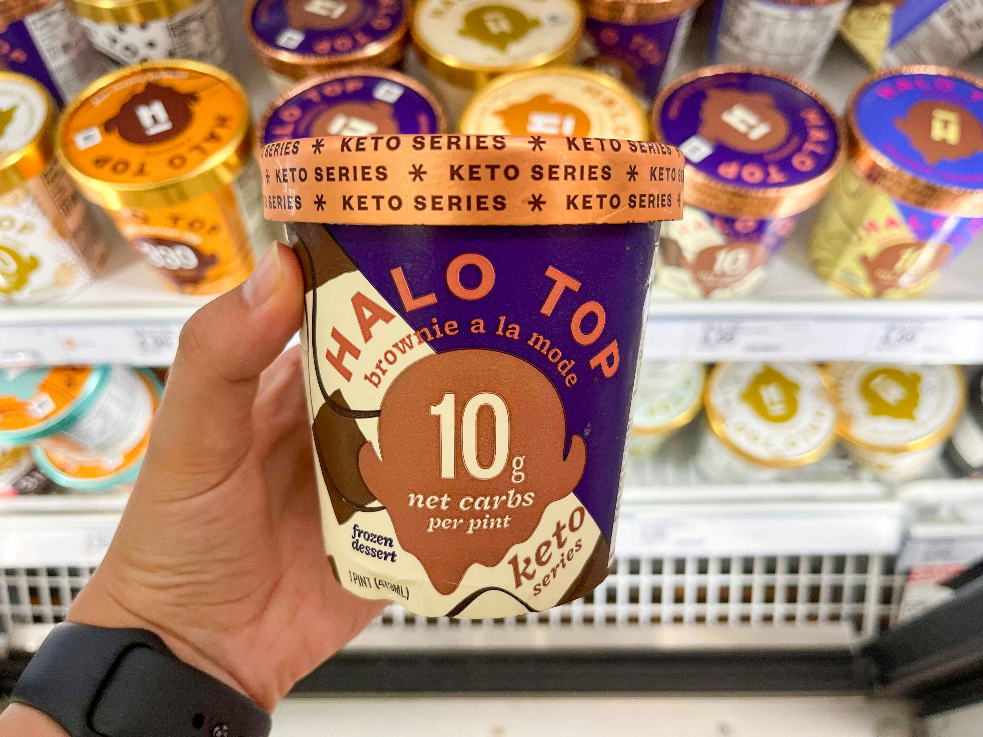 hang holding one pint of Halo Top ice cream in front of store freezer