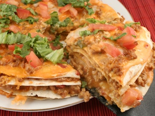 A homemade Mexican pizza with a quarter piece being taken from it