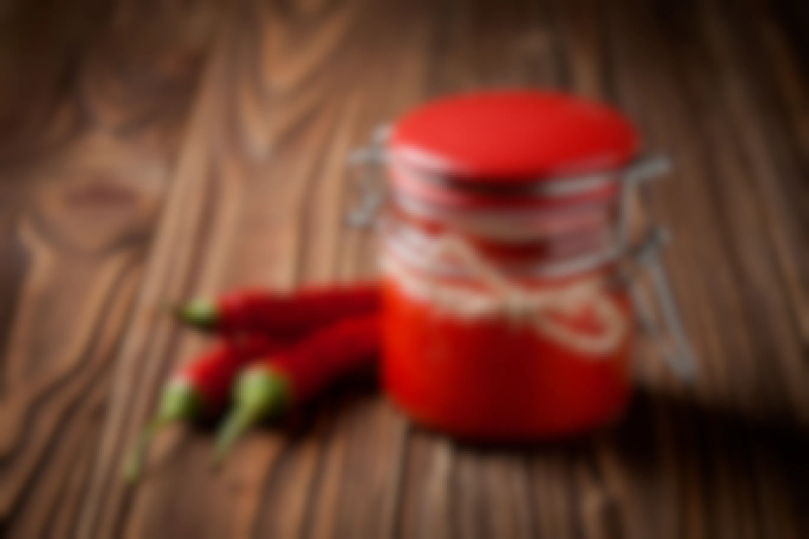 Jar of homemade sriracha sauce with chili peppers on a wooden table.