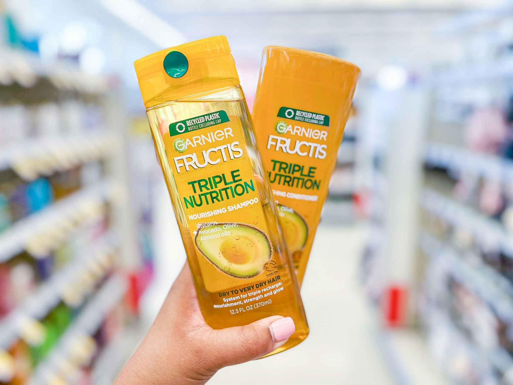Hand holding a bottle of Garnier Fructis Triple Nutrition Shampoo and Conditioner in aisle
