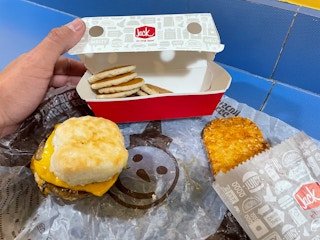 a person opening a pancake box with jack in the box breakfast on the table