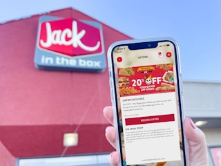 a person holding up a cellphone with app coupon in front of jack in the box store