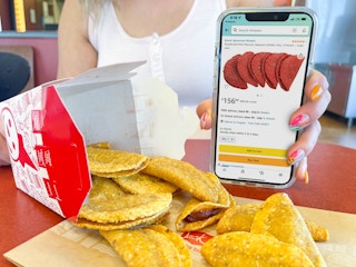 a woman holding a cellphone with amazon tacos on screen next too a box of mini taco spilling out