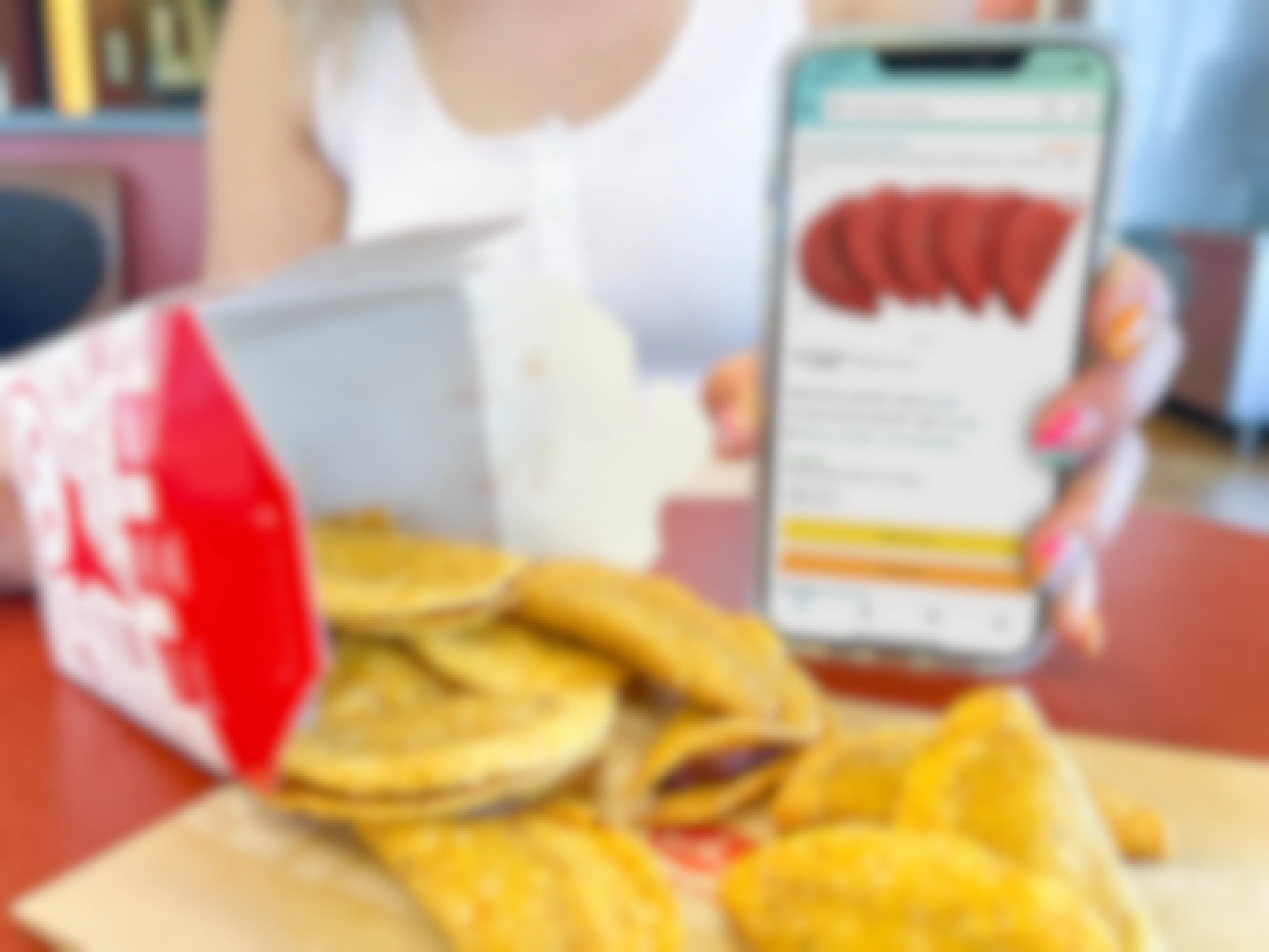a woman holding a cellphone with amazon tacos on screen next too a box of mini taco spilling out