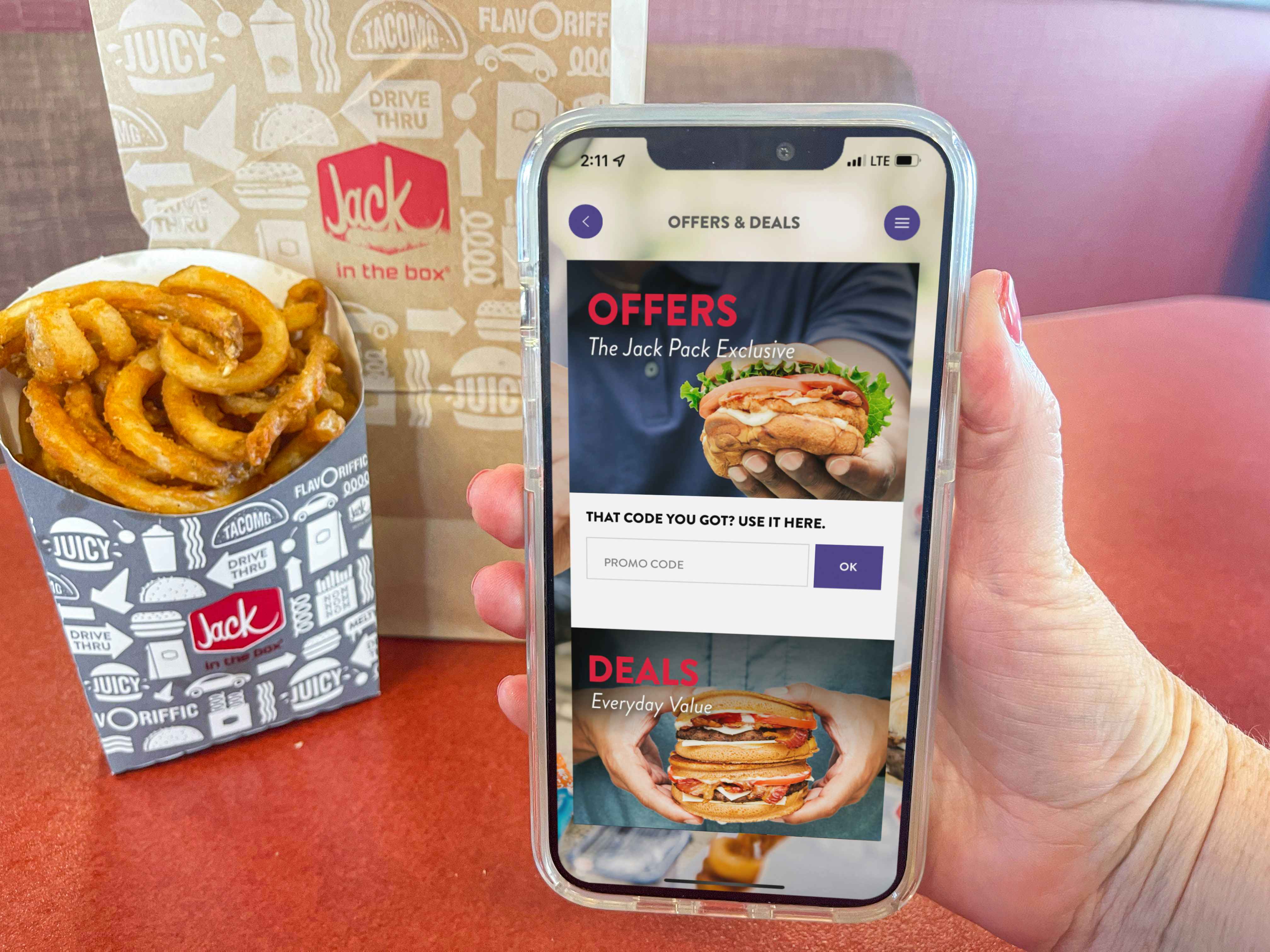 a person holding up a cellphone with app deals and offers page being held in front of french fries on table 