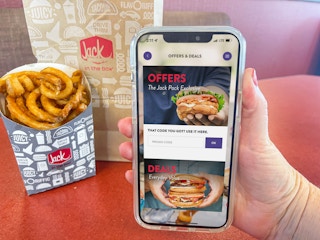 a person holding up a cellphone with app deals and offers page being held in front of french fries on table