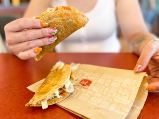 a jack in the box taco being held up with another laying on the wrapper sitting on the table