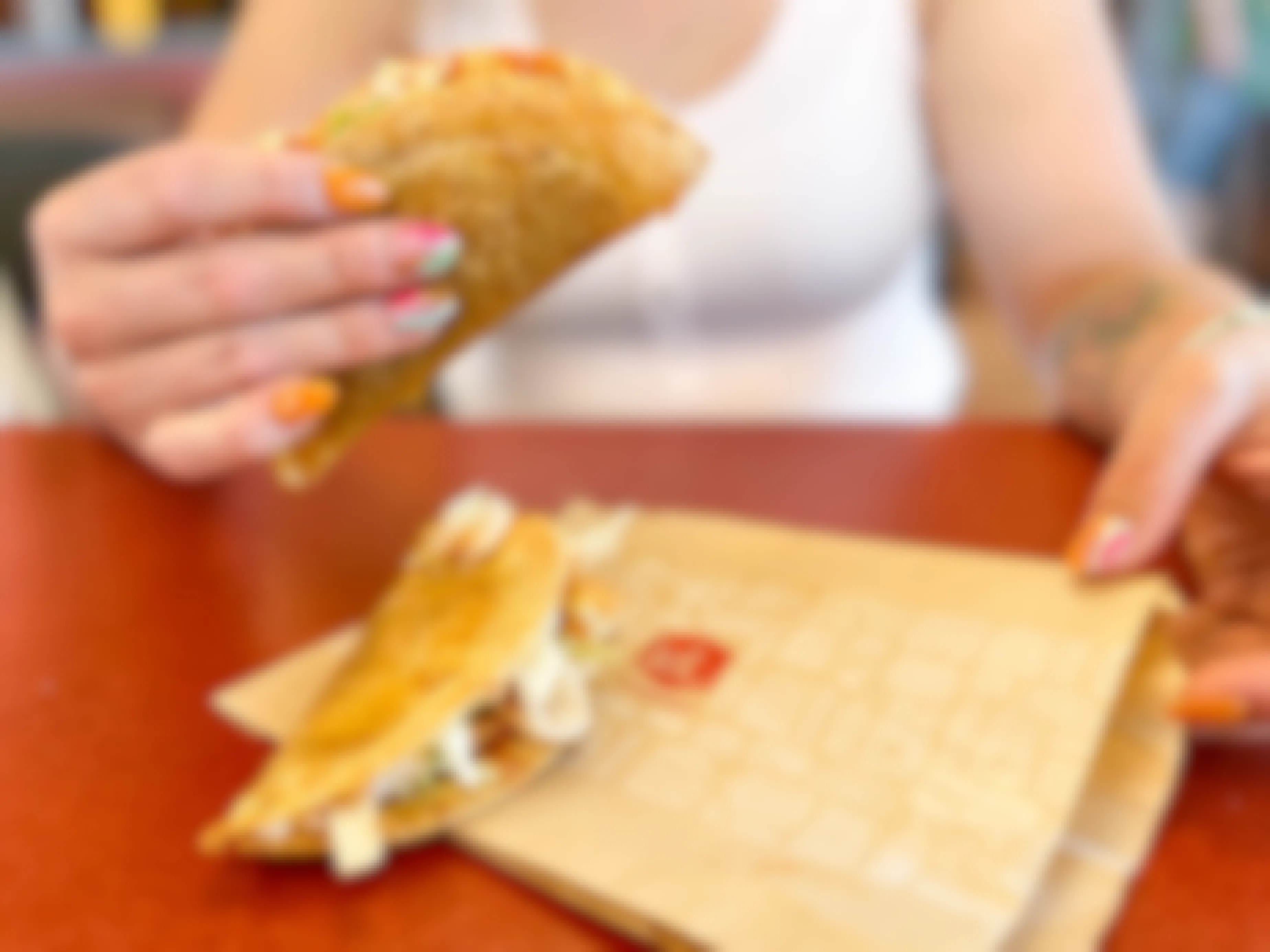 a jack in the box taco being held up with another laying on the wrapper sitting on the table