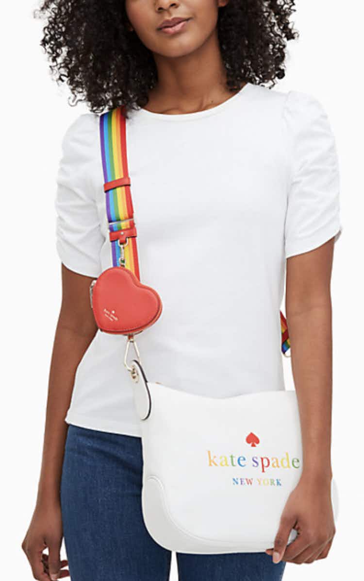 a woman wearing a white crossbody bag with a heart and rainbow details from kate spade