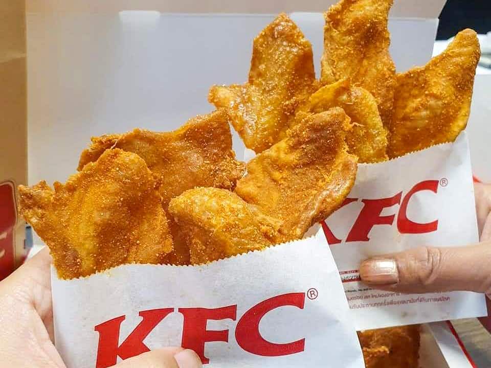 A person holding two white bags filled with chicken skins. The front of the bags has KFC written in large red letters. 