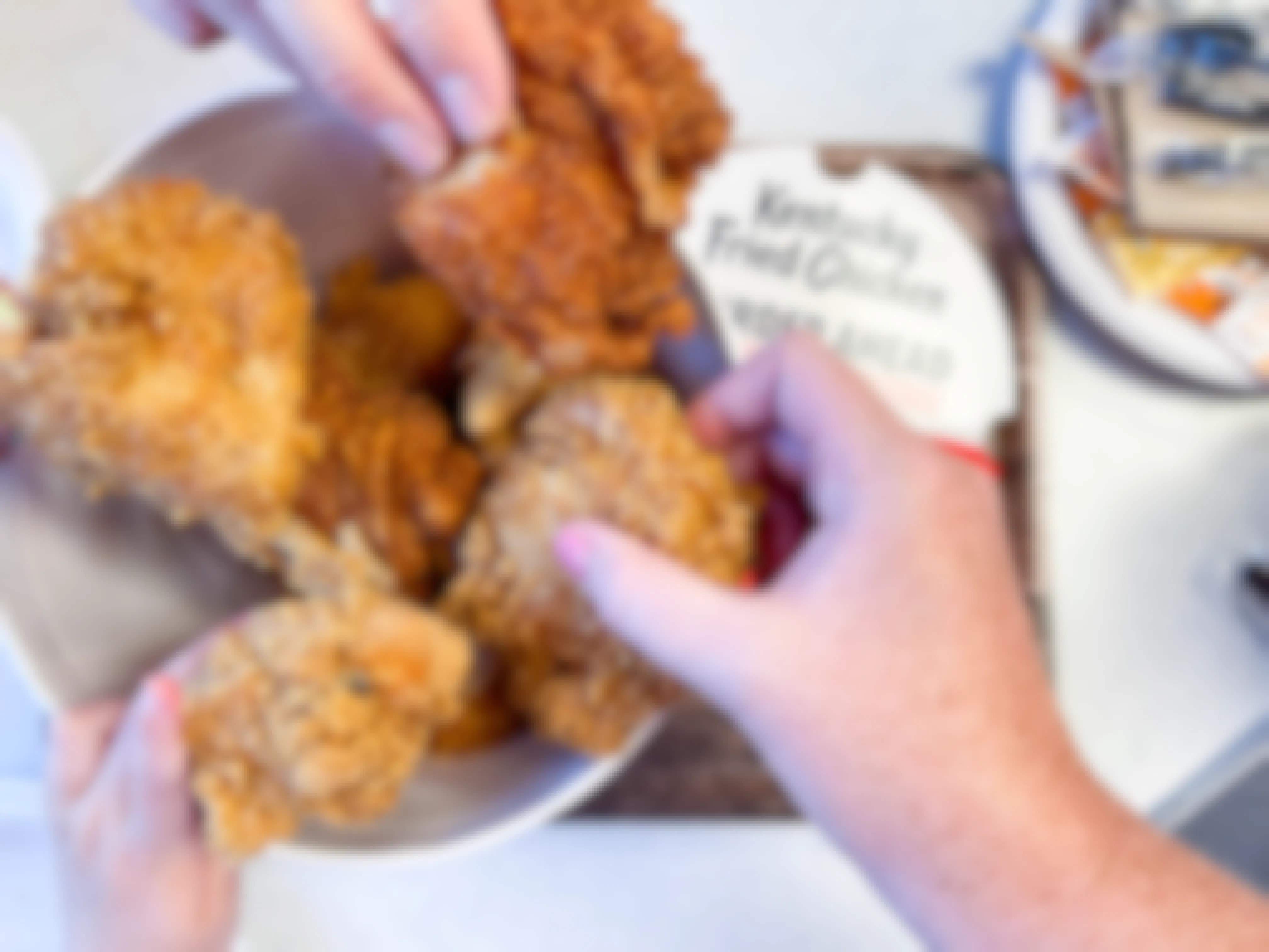 open bucket of kfc chicken on table with family hands pulling out multiple pieces of chicken