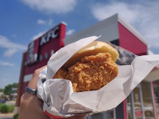 a person holding up a kfc chicken sandwich outside kfc