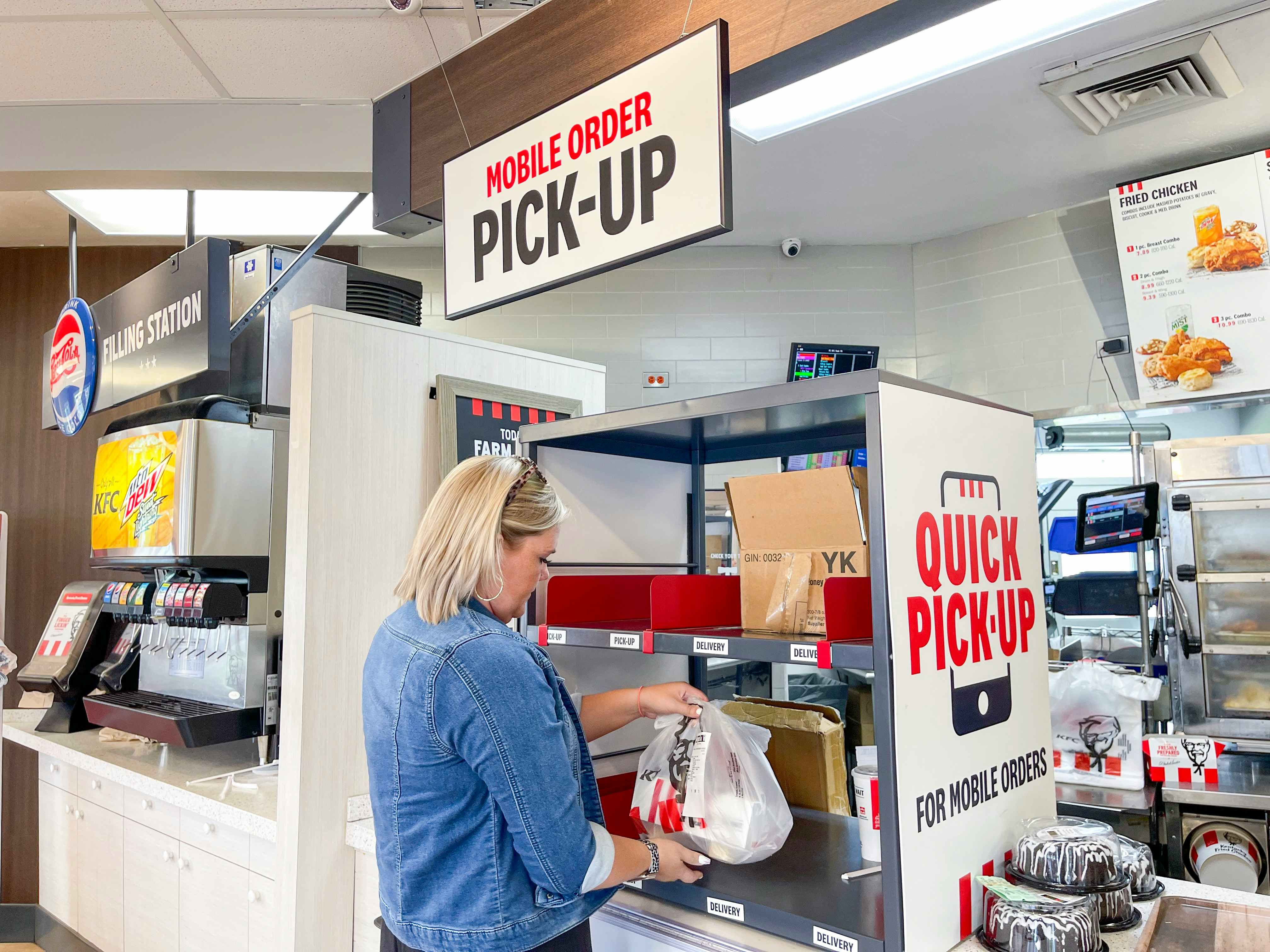 A woman standing at the pickup counter inside a KFC restaurant.