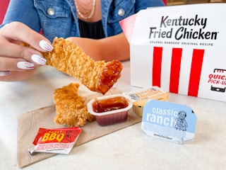 A person dipping a KFC chicken tender into a sauce container at KFC.