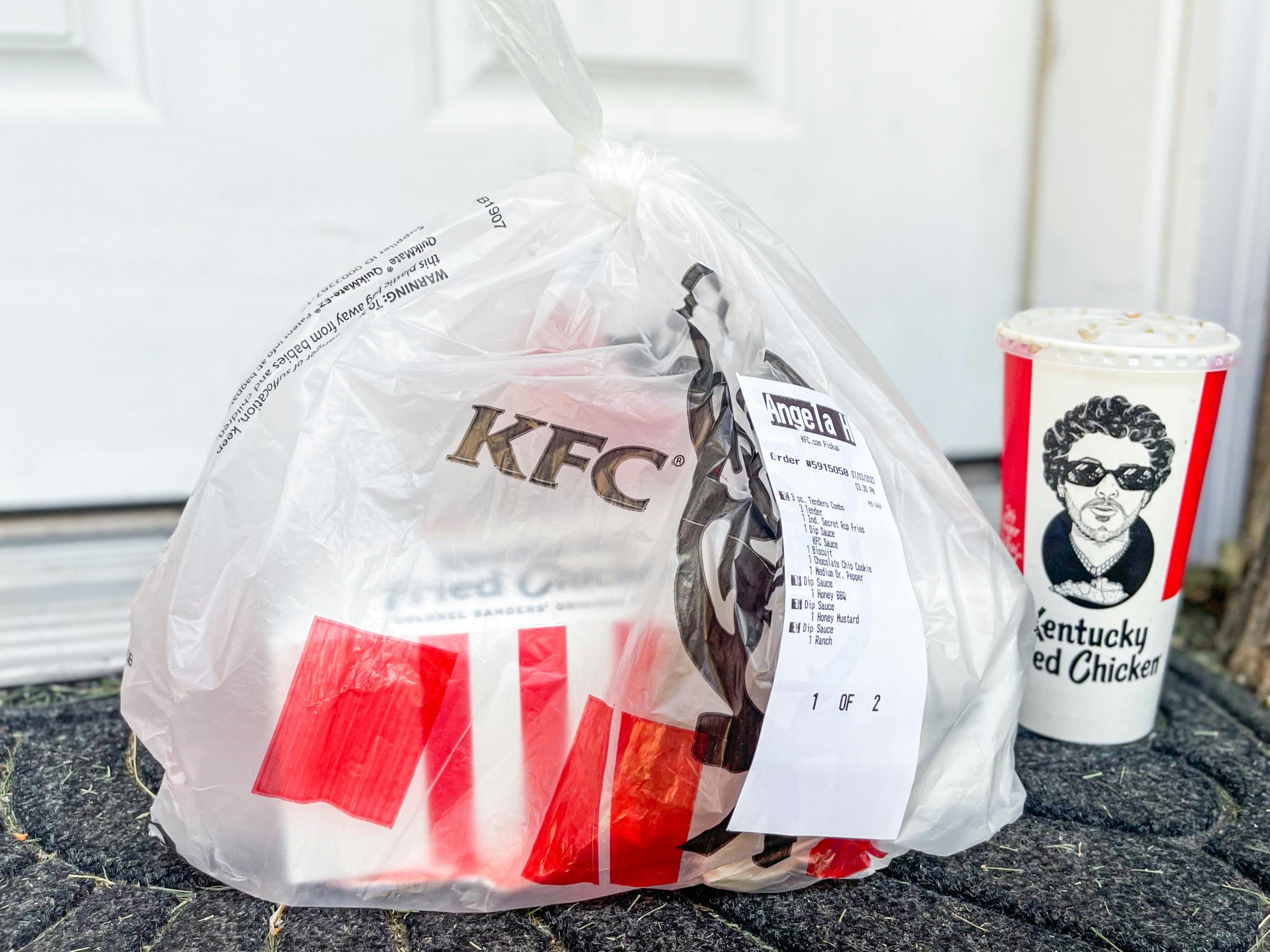 A bag of KFC takeout sitting on a front porch next to a drink.