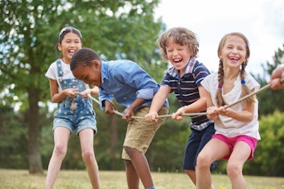Four children holding on to a rope, playing tug of war outside.