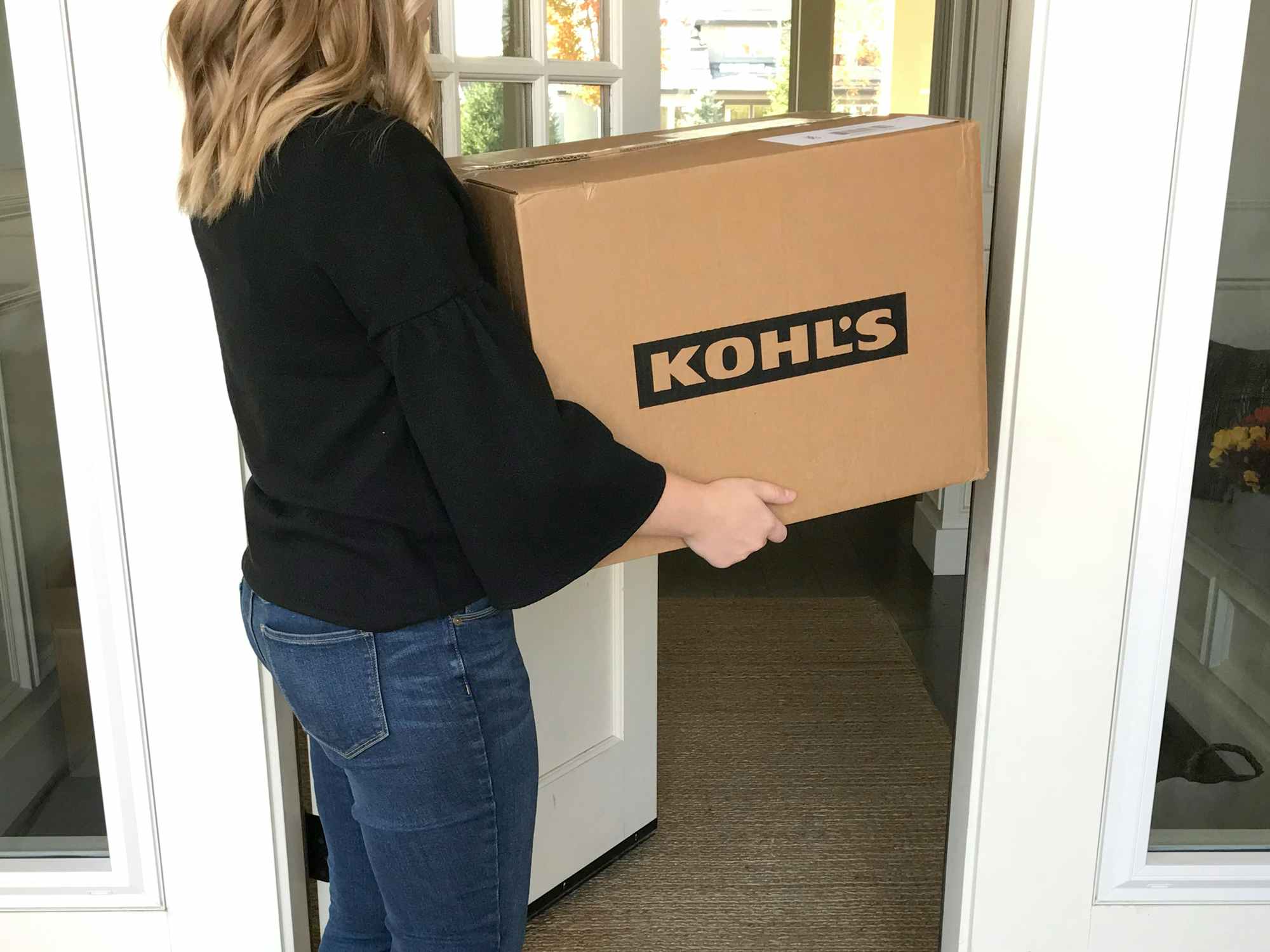 a person holding a kohls box walking into their house