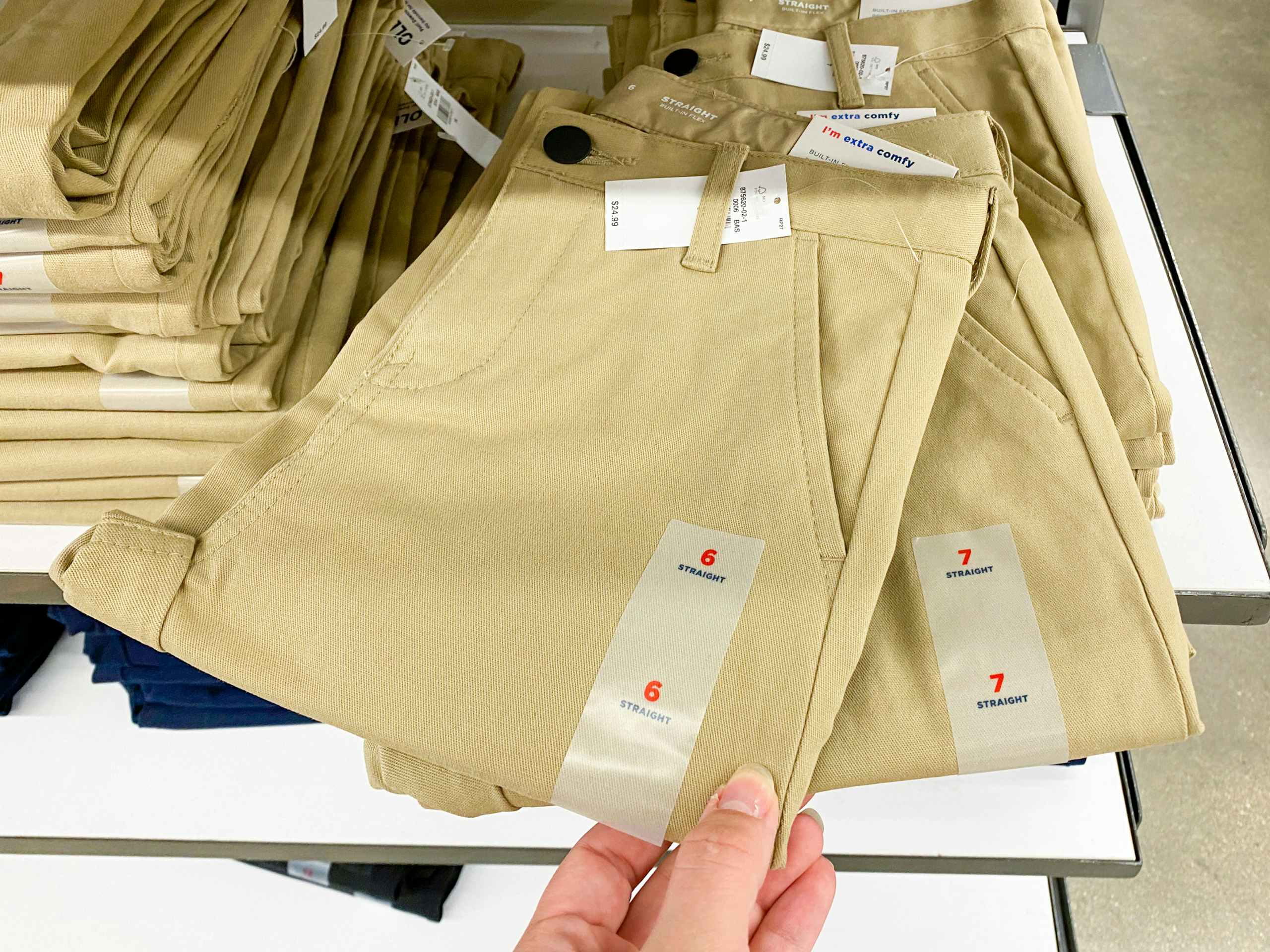 A person's hand taking a pair of children's school uniform pants from a shelf at Old Navy.