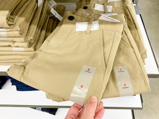 A person's hand taking a pair of children's school uniform pants from a shelf at Old Navy.