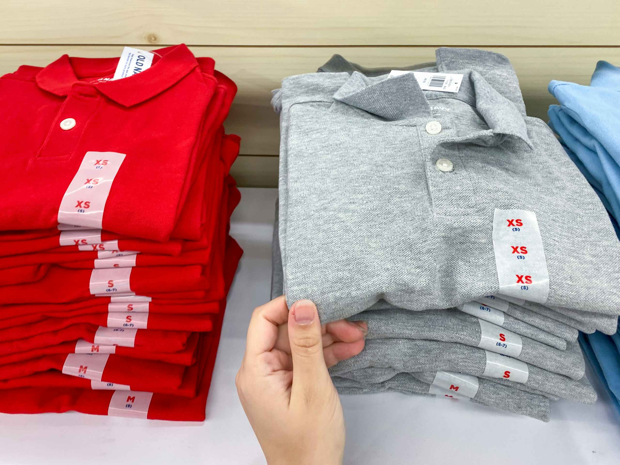 A person's hand taking a children's school uniform polo shirt from a shelf at Old Navy.