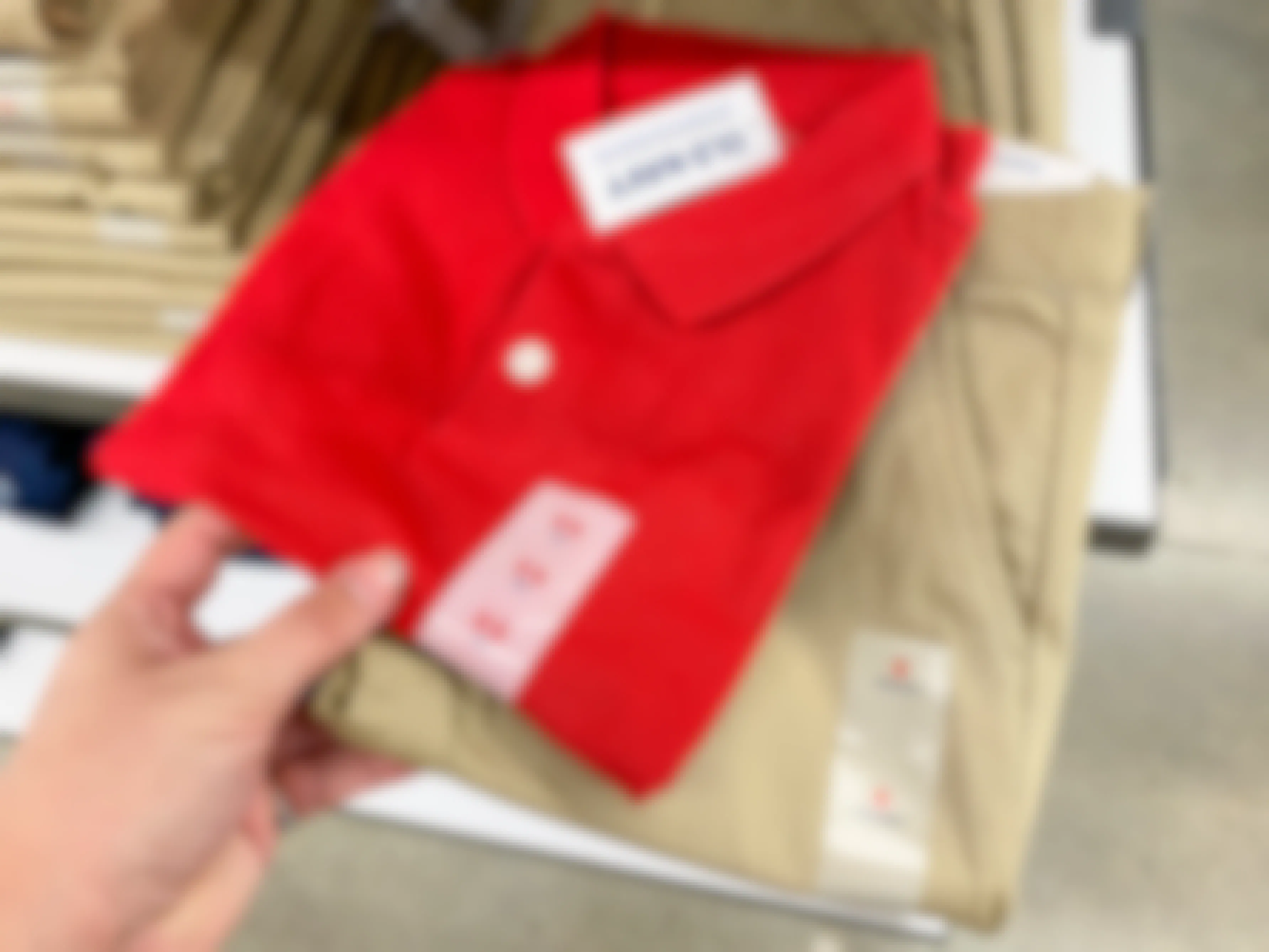 A person's hand taking a children's school uniform polo shirt and a pair of uniform pants from a shelf at Old Navy.