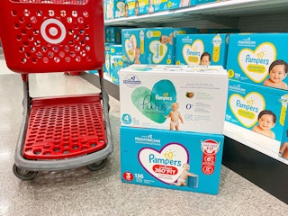 Two boxes of Pampers diapers stacked on the ground next to a Target shopping cart in the store aisle