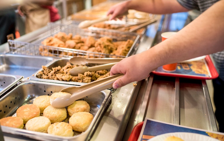 People serving themselves at a Popeyes chicken buffet.