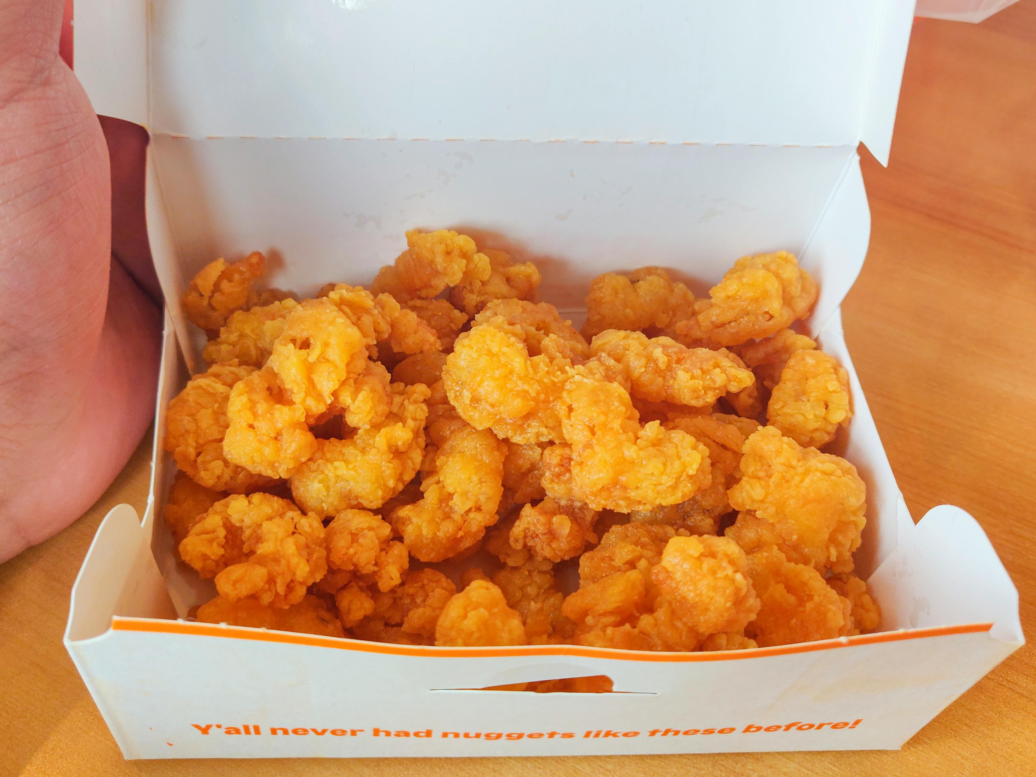 A box of Popeyes popcorn shrimp sitting on a table with a person's hand lifting the lid of the box.