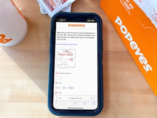 A Popeyes survey displayed on an iPhone that is on a table next to some Popeyes food containers.