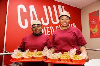 Two Popeyes employees carrying trays of Popeyes food.
