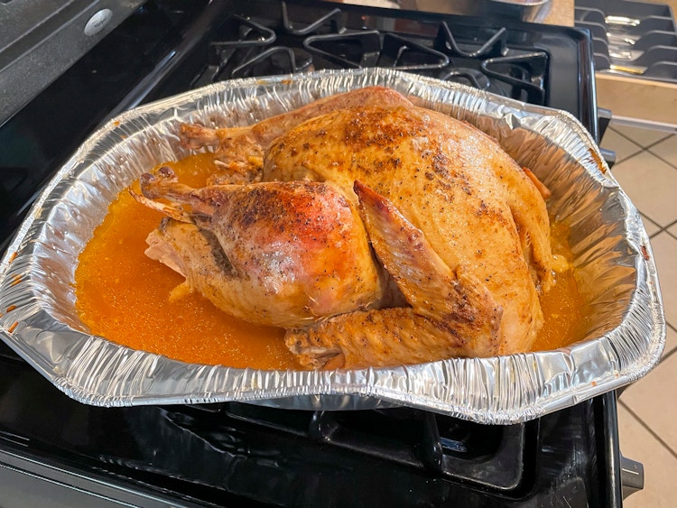 A cooked turkey in an aluminum baking dish, sitting on a stove.