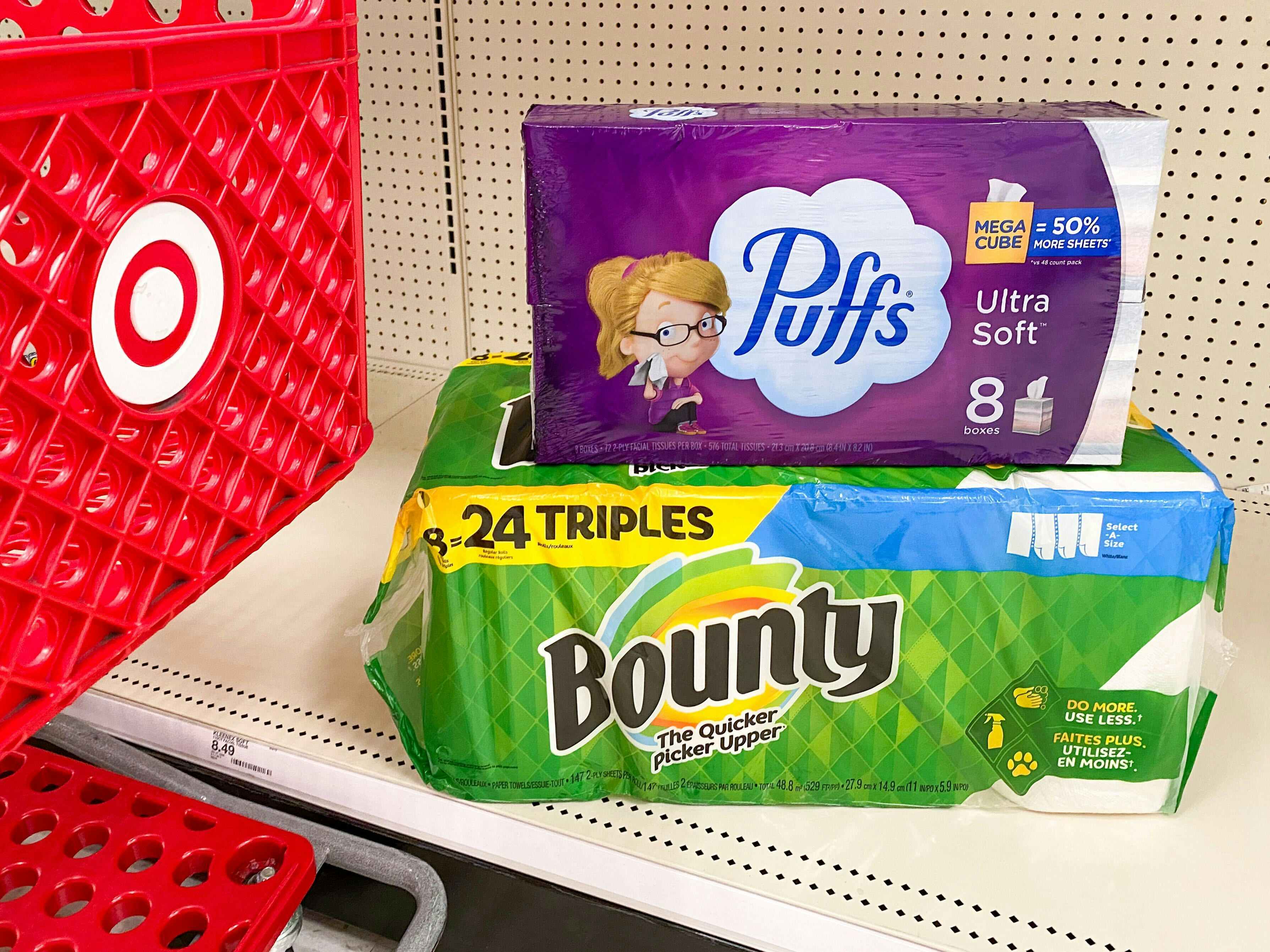 Bounty paper towels and puffs tissues are stacked on a store shelf next to a Target shopping cart