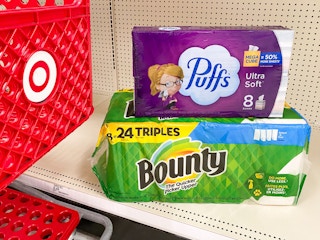 Bounty paper towels and puffs tissues are stacked on a store shelf next to a Target shopping cart