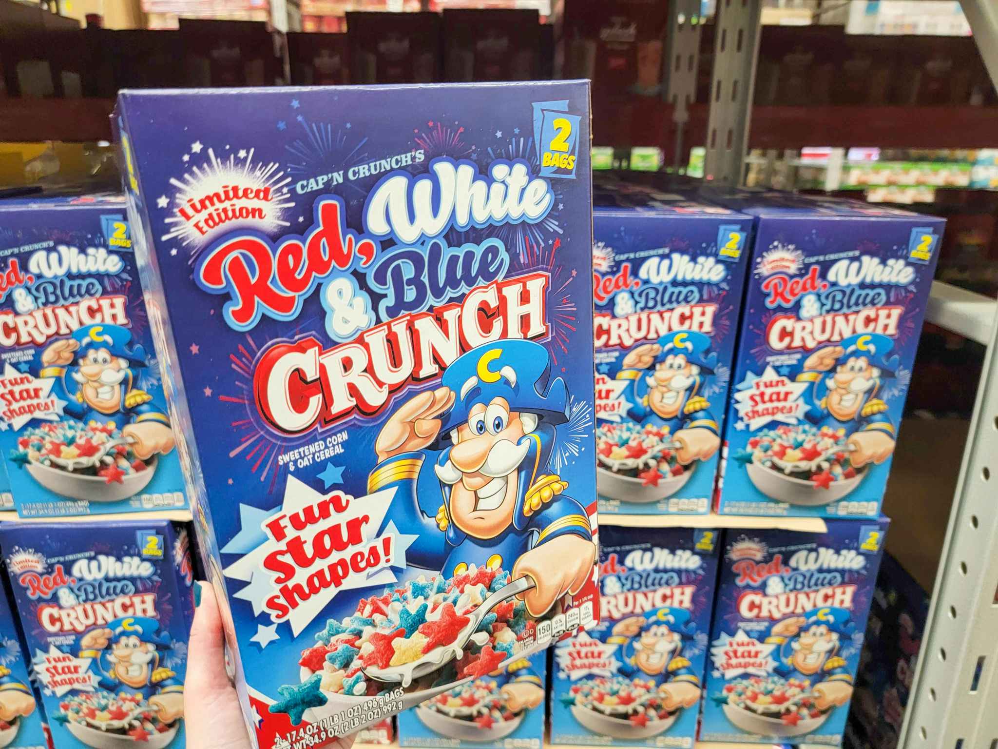 hand holding a box of red, white, and blue captain crunch cereal
