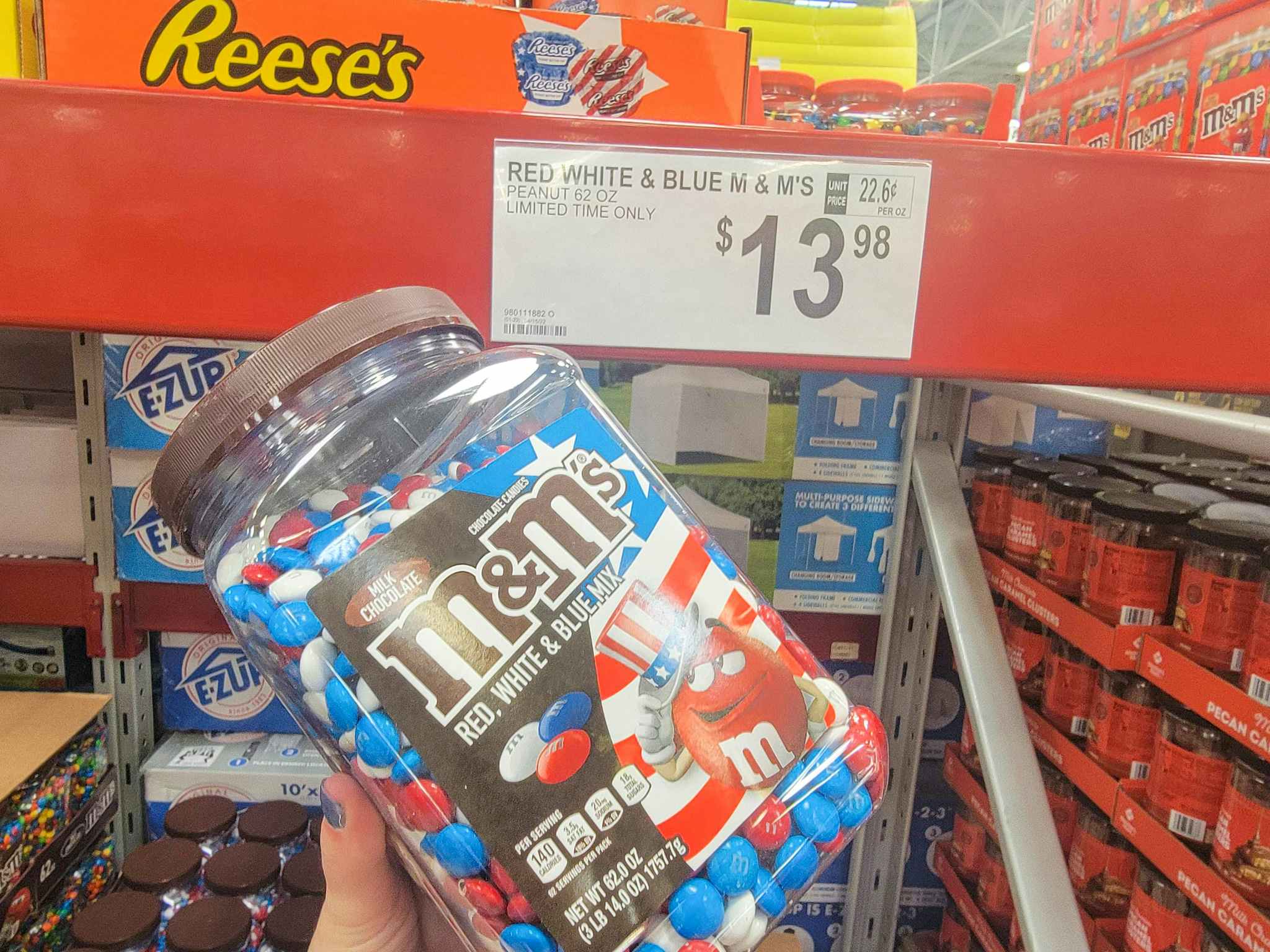 hand holding a large container of red, white, and blue m&m's