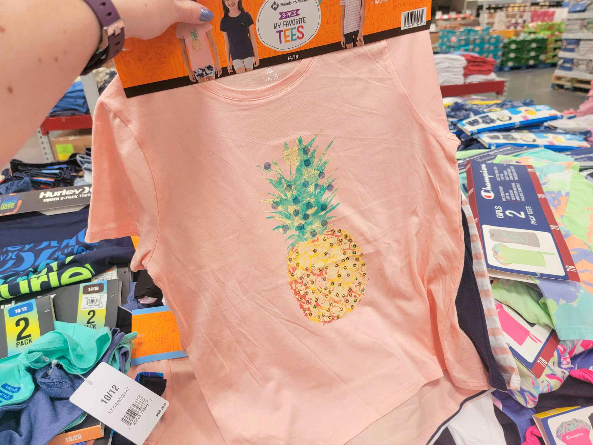 hand holding a set of 3 kids tees, the one in front is peach with a pineapple on it