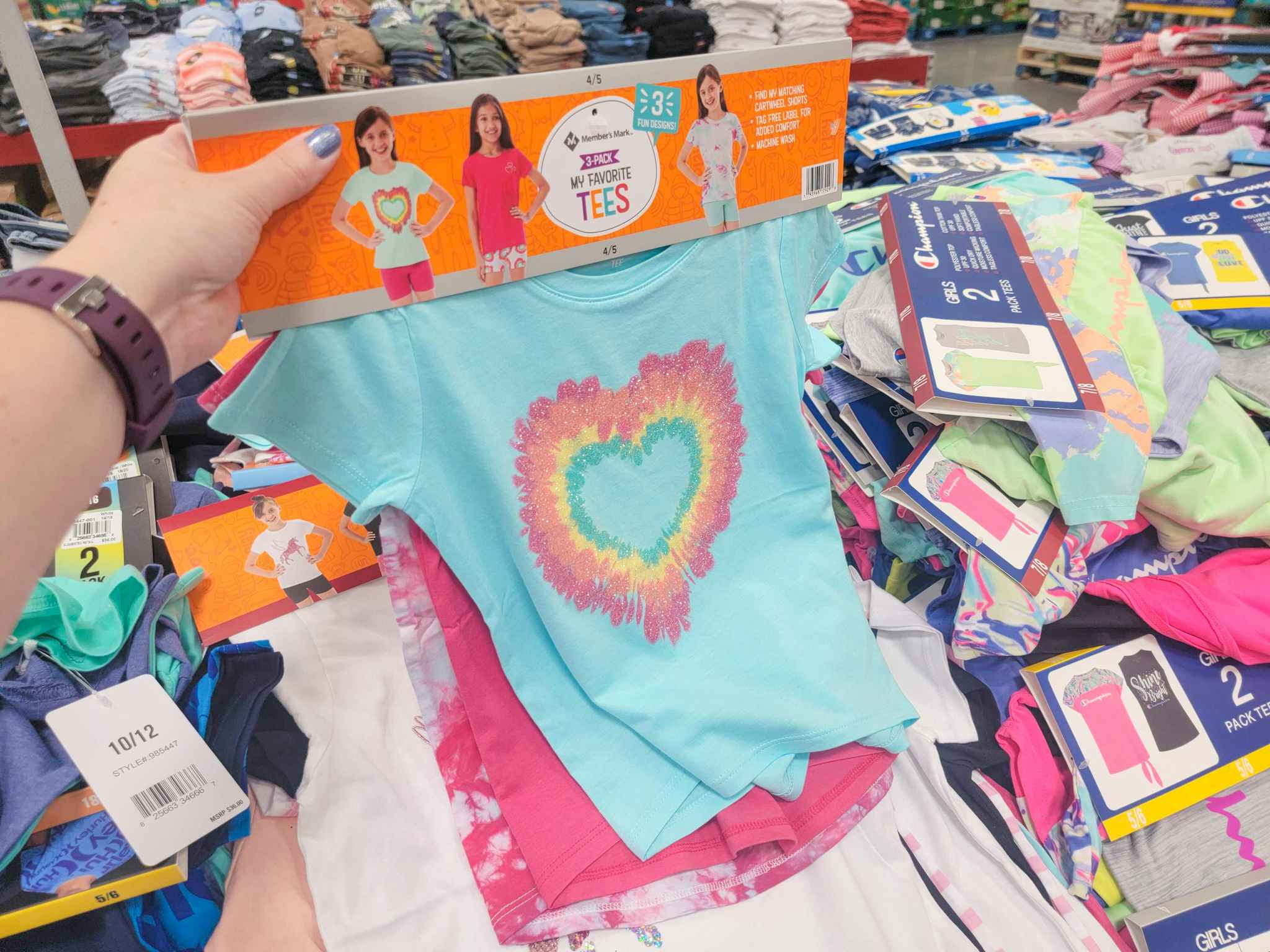 A hand holding a set of 3 kids tees. the front tee is teal with a heart