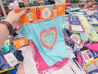 A hand holding a set of 3 kids tees. the front tee is teal with a heart