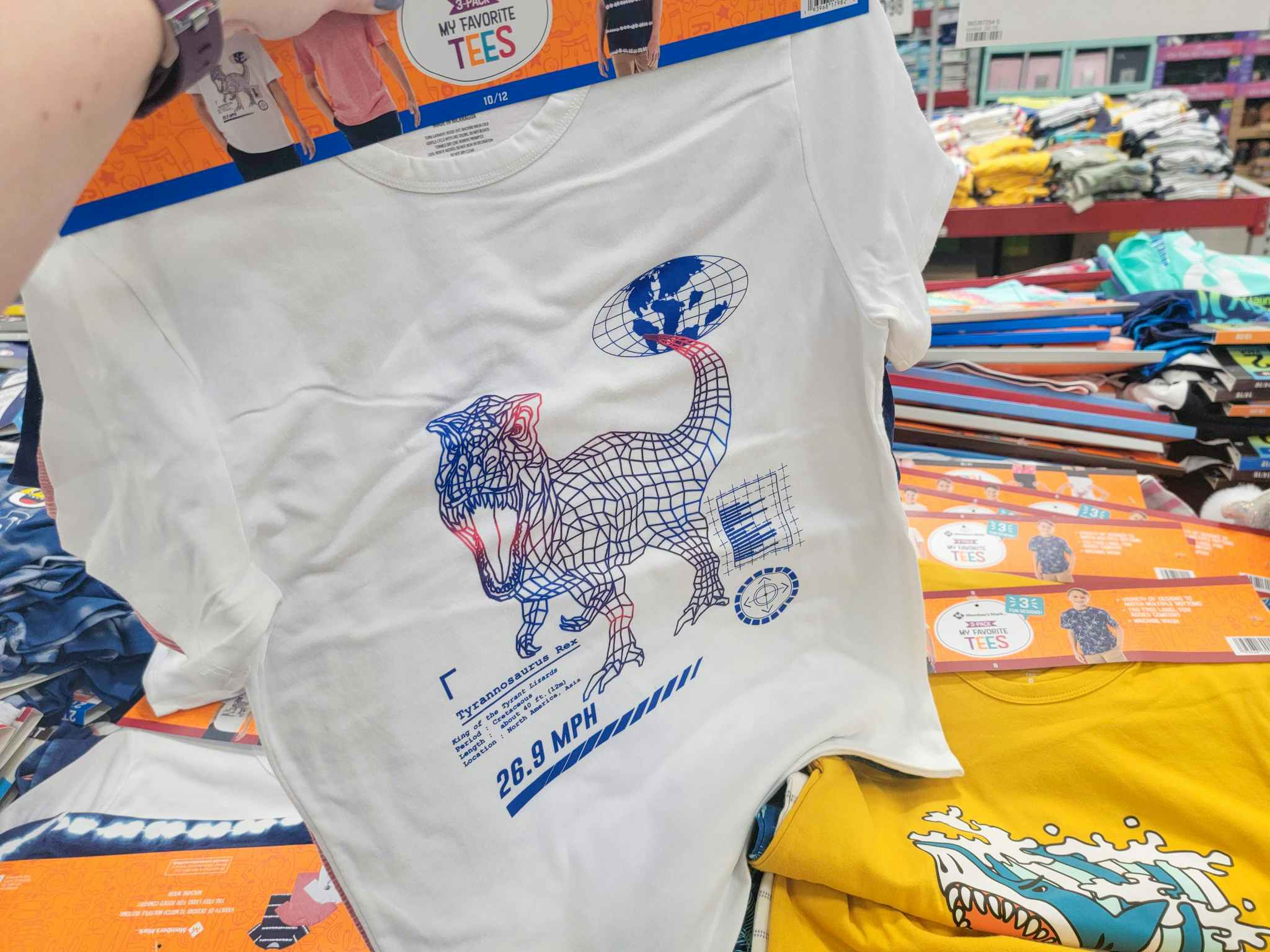 a hand holding a set of 3 kids tees. the front tee is white with a dinosaur