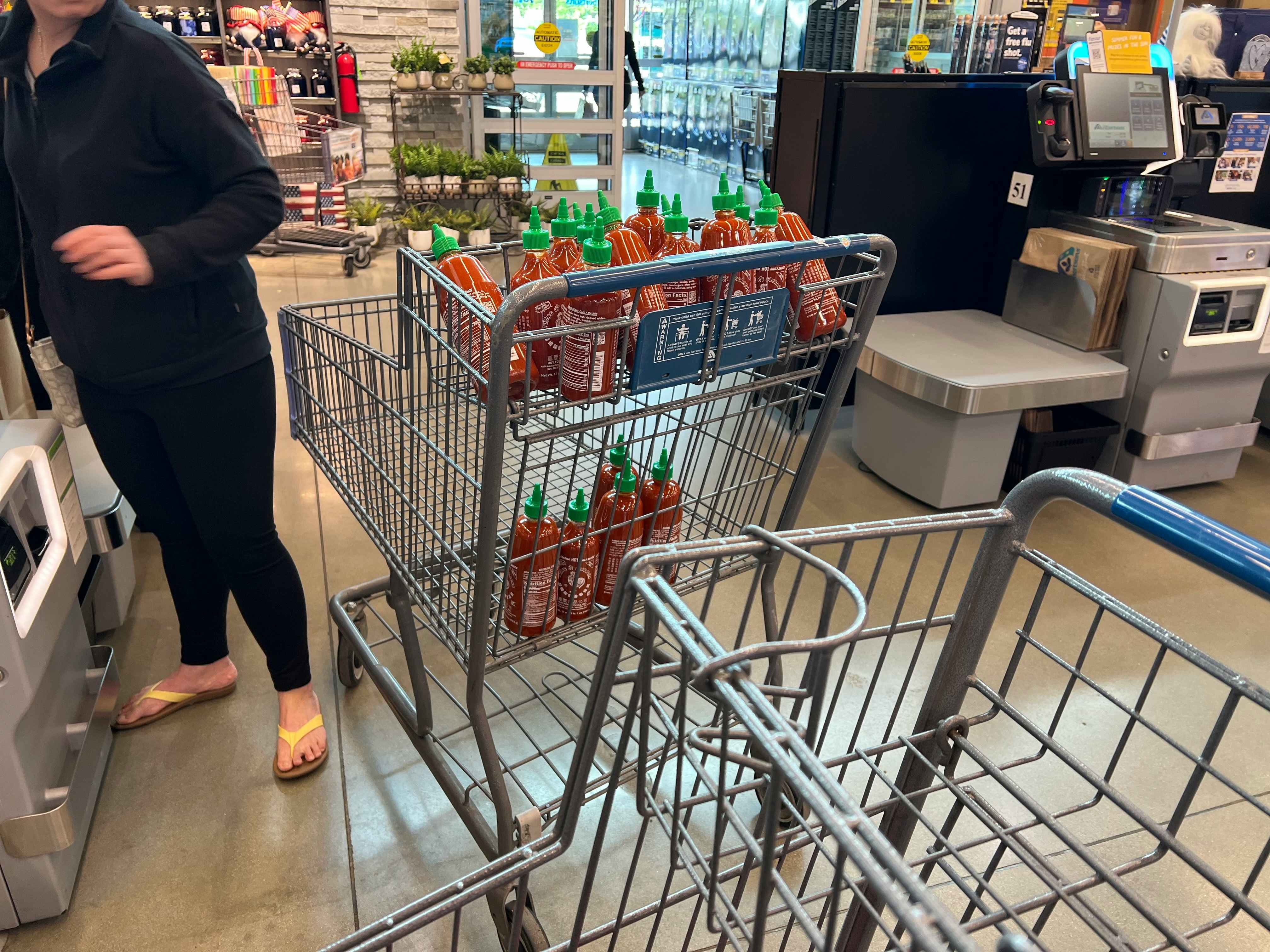 A customer with a cart full of Sriracha bottles in the line at Albertson's checkout.