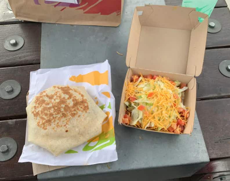 Taco Bell Crunchwrap and tostada on a table outside of Taco Bell.