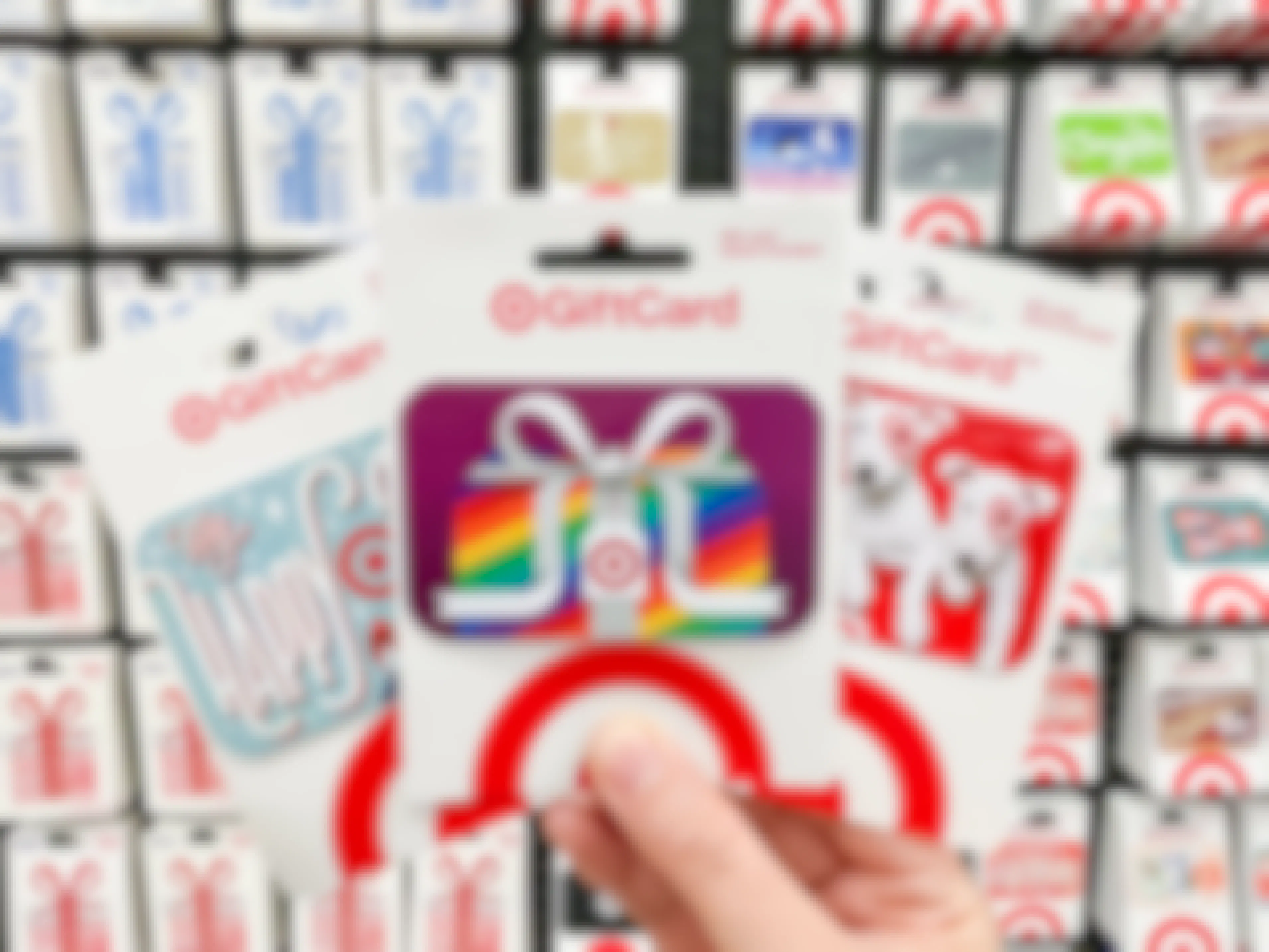 Three Target gift cards held in a person's hand in front of the wall of gift cards at Target.