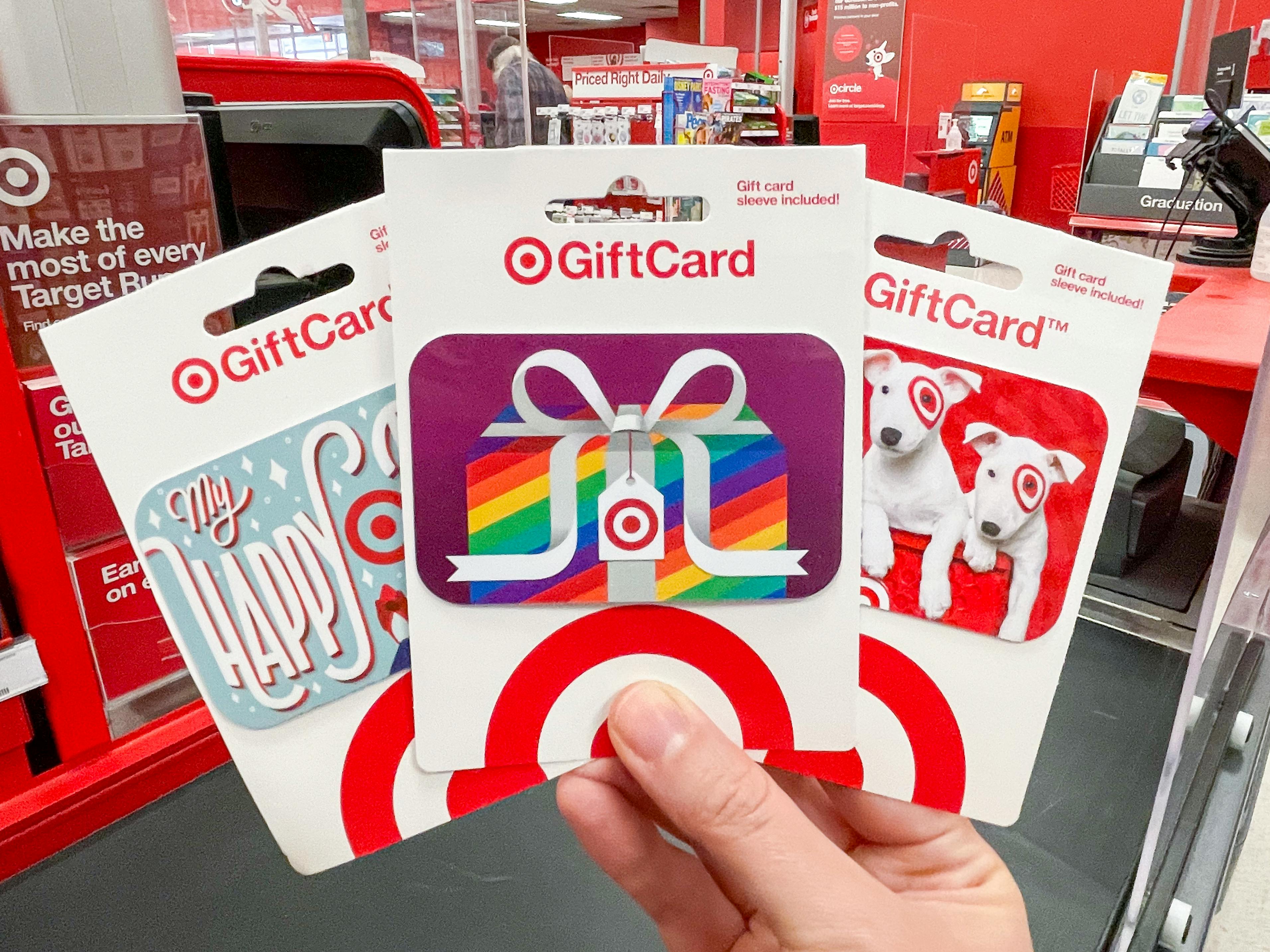 Three Target gift cards held in a persons hand at a checkout stand.
