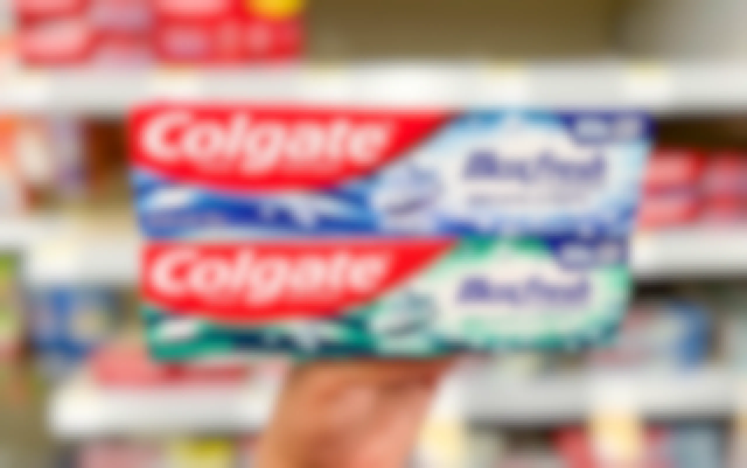 Hand holding two boxes of Colgate Maxfresh toothpaste in aisle